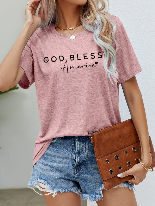 Person wearing a pink t-shirt with 'GOD BLESS America' text, holding a brown clutch.
